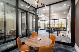 HQ on Main small meeting space inside of glass architectural walls with black frame round wood table with four orange chairs