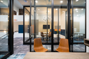 HQ on Main meeting space inside of glass architectural walls with black frame with two orange chairs