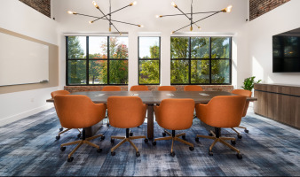 HQ on Main teleconference room with orange swivel chairs gold base and wood table with integrated technology natural light and modern ceiling pendant lighting