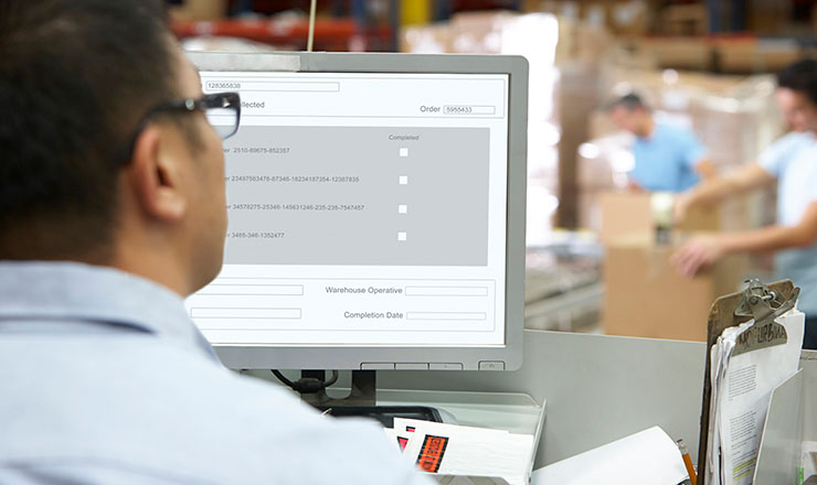 photo of a man looking at a computer screen inside of a warehouse